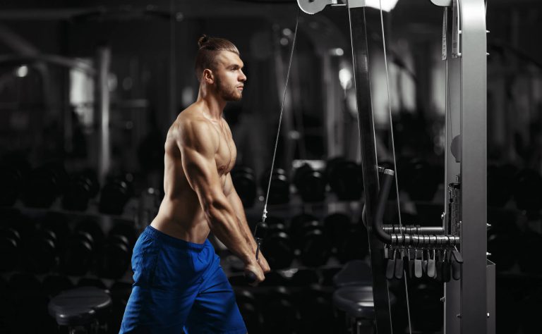 Man at cable machine fully engaged through his legs and core for tricep push-downs.